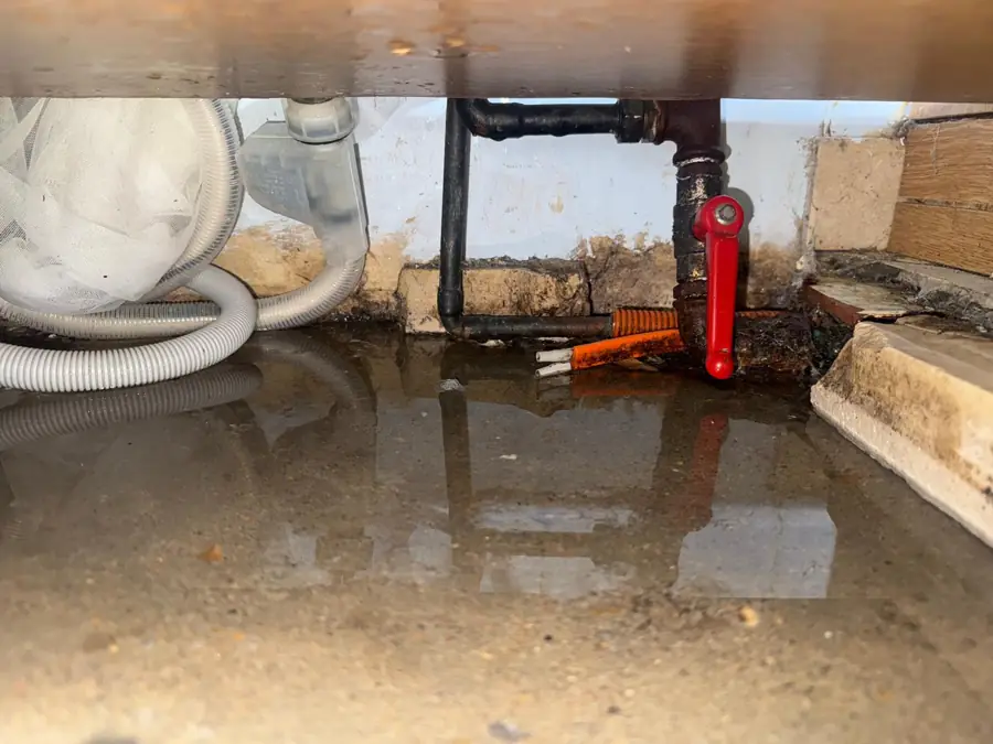 Fuite sous un meuble de cuisine : eau stagnante au pied des vannes